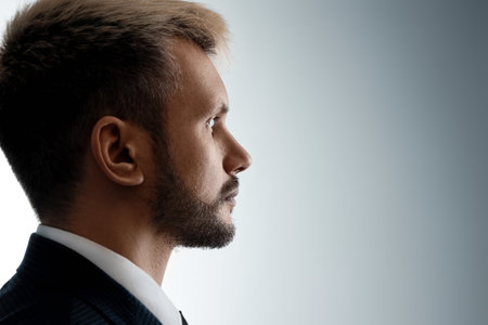 Close-up portrait of a man from his side in profile, looking at the light from the darkness. Neutral facial expression, copy spaceの写真素材
