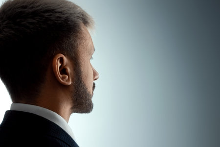 Close-up portrait of a man from his side in profile, looking at the light from the darkness. Neutral...