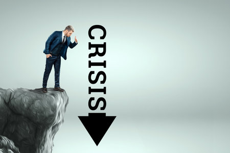 A man in a business suit stands on the edge of a cliff and looks down into an arrow with the inscription Crisis. Business concept, bankruptcy, problemsの写真素材