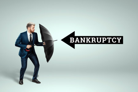 A man in a business suit stands with an umbrella in his hands and is defending himself from bankruptcy. Savings and assets protection, insurance conceptの写真素材