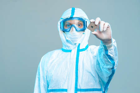 An employee holds a microchip in his hands, stands in a protective suit, glasses, a mask and gloves. Latest technologies, electronic microcircuit, computer security, neural networksの写真素材