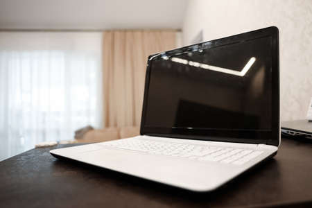 A laptop with a blank black screen in an angular position on a table against a blurred room background. The concept of workplace, office, coworkingの写真素材