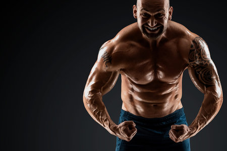 Male bodybuilder with light stubble and bare torso shows muscularity against a dark background. The concept of a fitness club, doing sports, weightlifting. Copy spaceの写真素材