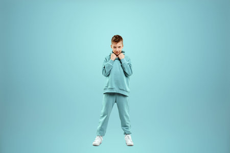 Little in a turquoise suit poses and fools around on a turquoise background, looks at the camera....