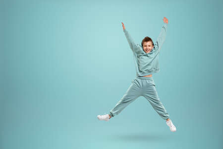Little in a turquoise suit poses and fools around on a turquoise background, looks at the camera. Children's studio portrait. Childhood lifestyle conceptの写真素材