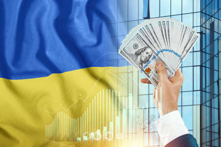 Money in a man's hand against the background of the flag of Ukraine. Income of Ukrainians. Financial condition of residents of Ukraine, taxes, loans, mortgages. State debt of the countryの写真素材