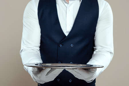 A male waiter in a white shirt and white gloves stands with a silver tray. The concept of service personnel serving customers in a restaurantの写真素材