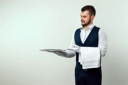 Handsome male waiter, in white shirt, holding a silver tray. The concept of serving staff serving customers in a restaurantの写真素材