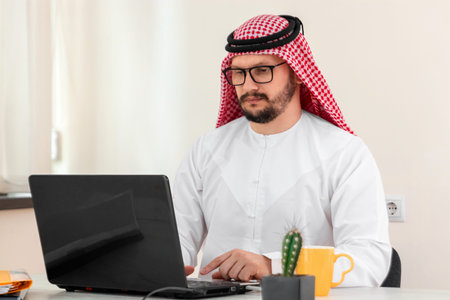An Arab man, a businessman, a sheikh works at a laptop. Investments, business, work via the...
