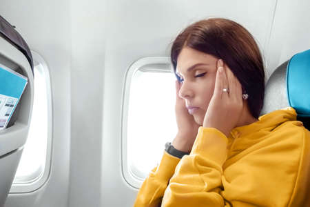 A girl sits in front of an airplane window and is nervous, afraid to fly, the cabin of a passenger airliner. Aerophobia, phobia, international flights, stress, motion sicknessの写真素材