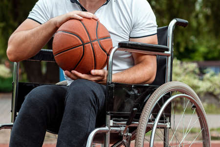 A man in a wheelchair plays basketball on the sports ground. The concept of a disabled person, a fulfilling life, a person with a disability, fitness, activity, cheerfulness.の写真素材