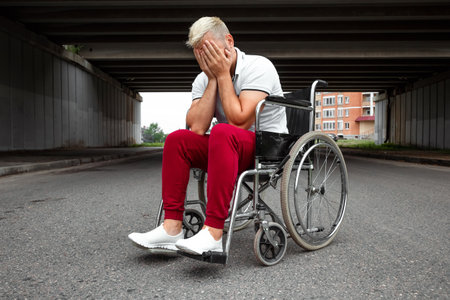 A man sits in a wheelchair, faced with difficulties alone, depression. The concept of a wheelchair, disabled person, full life, paralyzed, disabled person, health careの写真素材