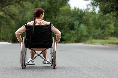 A young disabled girl sits in a wheelchair on the street. The concept of a wheelchair, disabled person, full life, paralyzed, disabled person, health careの写真素材