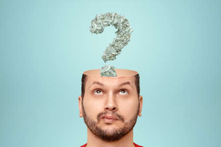 The man has question marks in his head made of banknotes, American dollars. The concept of financial crisis, bankruptcy, savings, fright, credit, debt, search for earningsの写真素材
