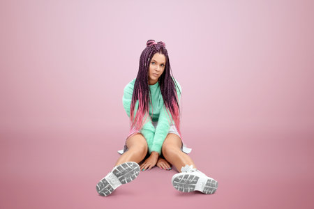 Millennial girl with pink braids hairstyle in turquoise clothes and sunglasses posing on a pink background. Concept for modern style, inclusiveness, individuality, generation Z, copy spaceの写真素材