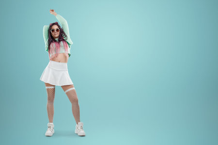 Millennial girl with pink braids hairstyle in turquoise clothes and sunglasses posing on a blue background. Concept for modern style, inclusiveness, individuality, generation Z, copy spaceの写真素材