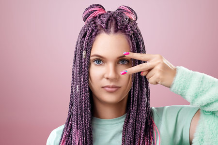Portrait of a beautiful girl with a hairstyle of pink braids in turquoise clothes posing on a pink...