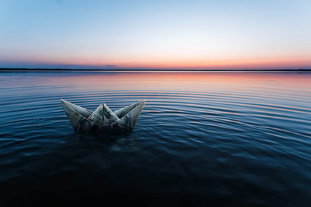A paper ship made from banknotes, made from dollars, floats in the water against the backdrop of a beautiful sunset. Origami from money, financial business model, copy spaceの写真素材