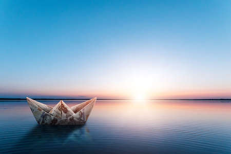 A paper ship made from banknotes, made from dollars, floats in the water against the backdrop of a beautiful sunset. Origami from money, financial business model, copy spaceの写真素材