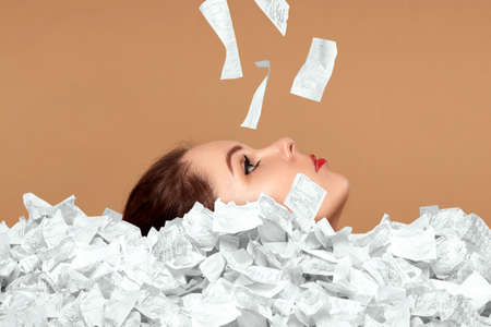 The face of a beautiful girl sticks out of a mountain of checks and bills. A person is drowning in debt, credit, mortgage, loan, mortgageの写真素材