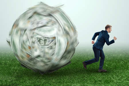 A ball made of dollars is rolling on a businessman. Financial crisis concept, debts, paying bills, mortgage, bankruptcyの写真素材