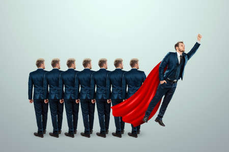 Uniqueness creative background, among the crowd of businessmen a man takes off with a red cloak. Competitive advantage, standing out from the crowd, thinking outside the box, a leaderの写真素材