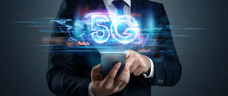 Creative background, a man's hand holds a phone with a 5G hologram on the background of the city. 5G network concept, high speed mobile internet, new generation networks. Mixed mediaの写真素材