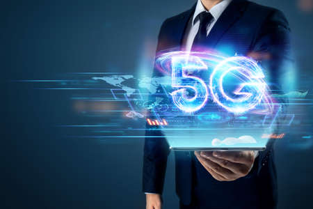 Creative background, a man's hand holds a phone with a 5G hologram on the background of the city. 5G network concept, high speed mobile internet, new generation networks. Mixed mediaの写真素材