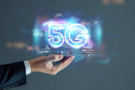 Creative background, a man's hand holds a phone with a 5G hologram on the background of the city. 5G network concept, high speed mobile internet, new generation networks. Mixed mediaの写真素材