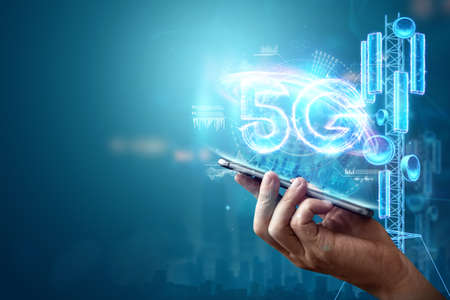 Creative background, a man's hand holds a phone with a 5G hologram on the background of the city. 5G network concept, high speed mobile internet, new generation networks. Mixed mediaの写真素材