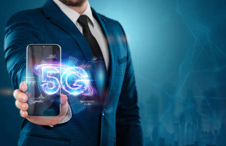 Smartphone glows 5G hologram, mobile technology, creative background. 5G network concept, high speed mobile internet, new generation networks. Mixed mediaの写真素材