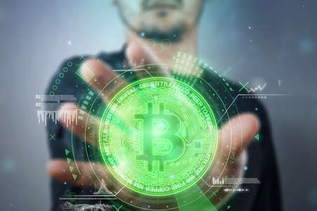 In the hand of a businessman a bitcoin coin with analytics data, electronic money. Blockchain transfer concept, cryptocurrency, data encryption. Mixed mediaの写真素材