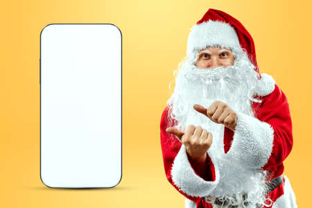 Smartphone mockup image, environment to showcase mobile app design, creative background. Smartphone for your advertising. Santa claus is standing next to a large smartphone. Christmas advertisementの写真素材