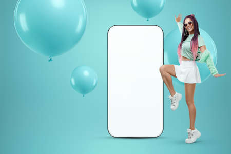 White screen smartphone mockup, environment to showcase mobile app design, creative background, smart phone for your advertisement. A creative girl stands next to a large smartphone. Copy spaceの写真素材