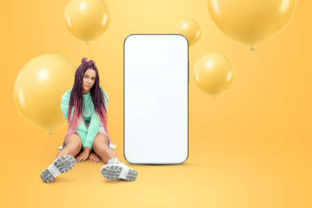 White screen smartphone mockup, environment to showcase mobile app design, creative background, smart phone for your advertisement. A creative girl stands next to a large smartphone. Copy spaceの写真素材