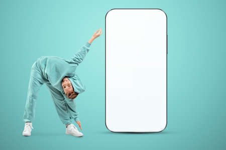 The boy is standing near a large smartphone with a white screen. Copy space, mixed media, ad layout, empty design environment, creative backgroundの写真素材