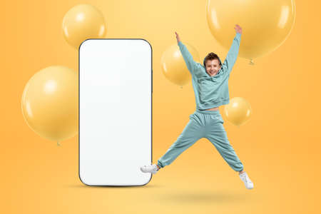 White screen smartphone mockup, environment to showcase mobile app design, creative background, smart phone for your advertisement. A cheerful boy stands next to a large smartphone. Copy spaceの写真素材