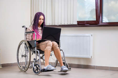 Beautiful modern disabled girl working on a laptop in a wheelchair. Work from home, work for the disabled, freelancing, remote workの写真素材