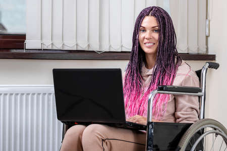 Beautiful modern disabled girl working on a laptop in a wheelchair. Work from home, work for the disabled, freelancing, remote workの写真素材