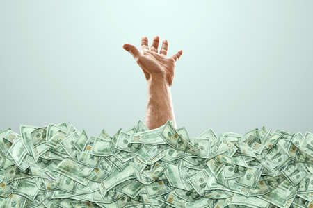A human hand sticks out of a pile of money, a lot of dollars. The concept of a successful business, jackpot, win.の写真素材