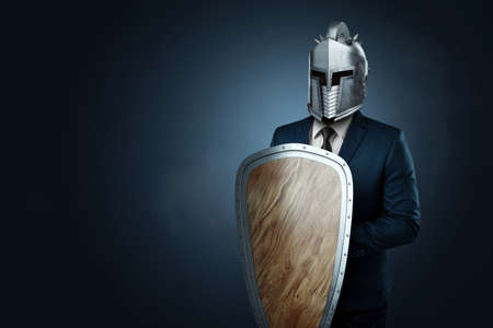 Creative image, a man in a modern suit of a businessman, a knight's helmet on his head, armor. The concept of a modern hero, overcoming difficulties, a crisis, a good manager. magazine style.の写真素材