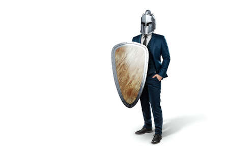 Creative image, a man in a suit of a businessman, a knight's helmet on his head on a white background. The concept of a modern hero, overcoming difficulties, crisis management. magazine style.の写真素材
