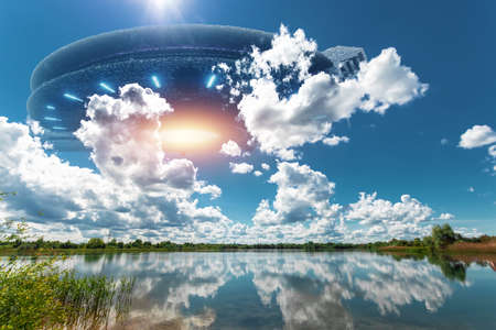 UFO, an alien saucer hovering above the lake in the clouds, hovering motionless in the sky. Unidentified flying object, alien invasion, extraterrestrial life, space travel, spaceship. mixed media.の写真素材