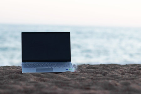 The laptop is lying on the sand on the beach. The concept of working online anywhere