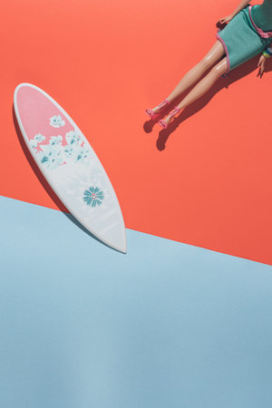 Doll on an orange-blue background with a surfboard. Minimal composition.の写真素材
