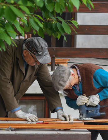 Elderly couple cutting wood together with power toolsの写真素材