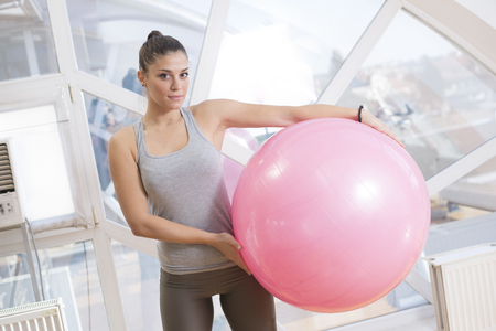 Girl staning in a gym holding pink fitness ballの写真素材