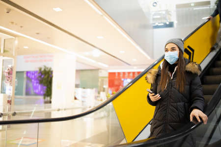 Young woman with a protective mask taking the stairs in a shopping mallの写真素材