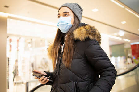 Young woman with a protective mask taking the stairs in a shopping mallの写真素材