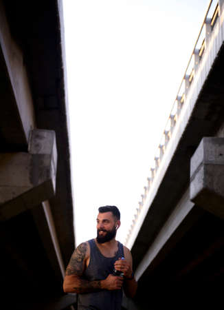 Young modern man with a beard taking a pause during his exercising outdoors in the streets to hydrate himselfの写真素材